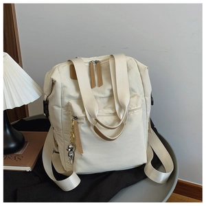 Detalle de una mochila de lona beige con correas de cuero marrón y un colgante de oso