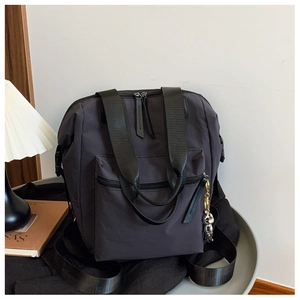 Detalle de mochila de nailon gris oscuro con asas anchas y colgante metálico lateral