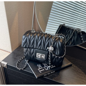 Detail of black matelassé chain bag with silver turn-lock and engraved metal orb charm