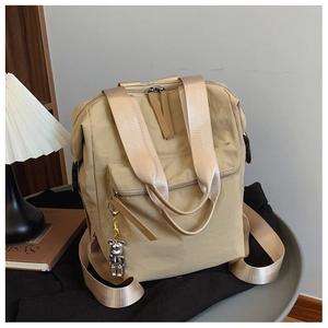 Detalle de mochila de nailon beige con bolsillo frontal y colgante de oso robot plateado