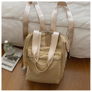Detalle de la mochila de nailon beige con hebillas laterales y un colgante de oso plateado