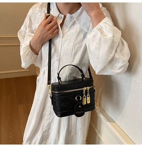 Close-up of black crossbody box bag with embossed letters and gold zipper detail