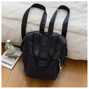 Detalle de mochila de nailon negro con cremallera, hebillas laterales y colgante de astronauta