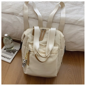 Detalle de mochila de nailon blanco crema con bolsillo frontal y colgante de oso plateado