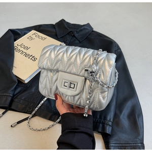 Close-up of silver quilted crossbody bag with metal twist lock and chain strap detail