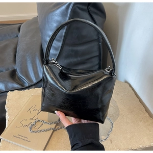 Detail of black glossy pleated bucket bag with silver chain strap and top handle