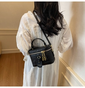 Detail view of black lychee grain cylinder bag with golden zippers and detachable strap