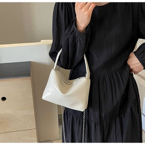 Detail view of cream white patent leather bucket bag with silver chain on black dress