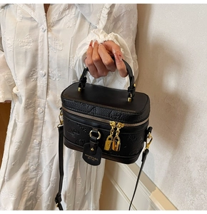 Detail of black cylindrical vanity bag with textured leather and gold hardware