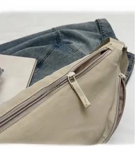 Close-up of smooth nylon zipper and durable ripstop fabric on a beige crossbody bag