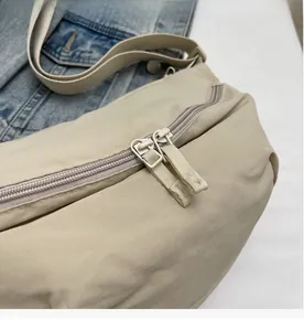 Detailed close-up of smooth dual zippers on a beige canvas dumpling crossbody bag