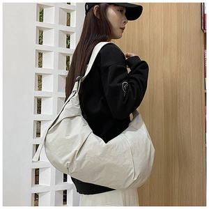Side view of a large cream nylon crescent bag worn by a model for a casual commute look