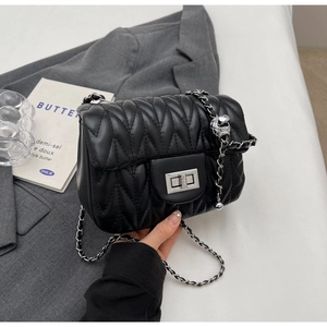 Detail of black quilted crossbody bag with silver metal chain and rotary lock clasp