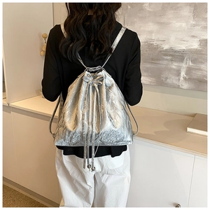 Silver metallic drawstring bucket backpack shown on model in a modern interior setting