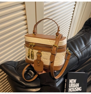 Detail of cream embossed box bag with brown leather handles and golden zipper closure