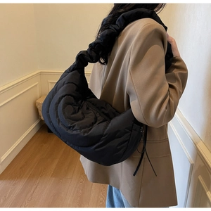 Detail of black quilted cloud bag with spiral stitching and ruffled strap on shoulder