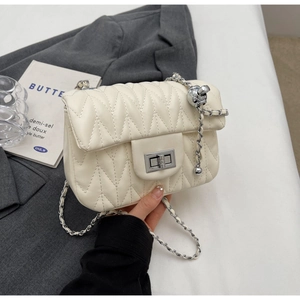 Detail of off-white quilted crossbody bag featuring silver chain and metal ball charm