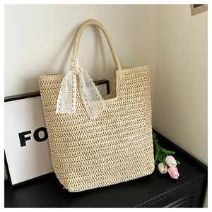 Detail of woven straw tote bag featuring white lace bow on the handle in a minimalist setting