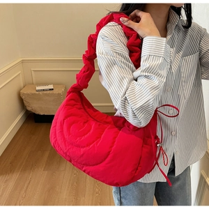 Detail of vibrant red quilted nylon crescent bag with ruched strap on striped shirt