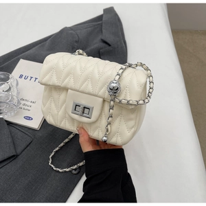 Detail of off-white quilted crossbody bag with silver chain strap and metal ball adjuster