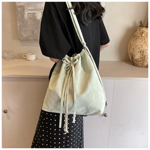 Detail view of light green bucket bag with drawstring bow and metal bead charm on model