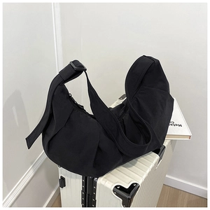 Detail of a black hobo bag with nylon texture on a white suitcase in minimalist setting