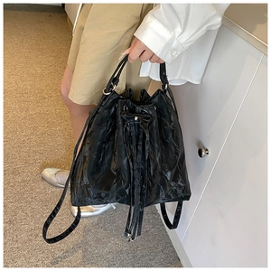 Detail of black drawstring bucket bag with glossy pleated texture and shoulder strap