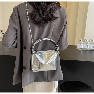 Detailed view of shiny silver metallic bucket bag with chain strap on grey blazer