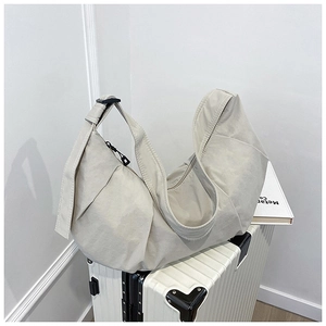 Close-up of beige crescent bag on luggage showing durable nylon fabric and wide strap