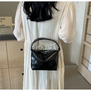 Detail of glossy black bucket bag with metallic chain strap and top handle on a model