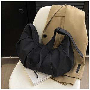 Detail of black pleated hobo bag with adjustable strap on white chair and blazer
