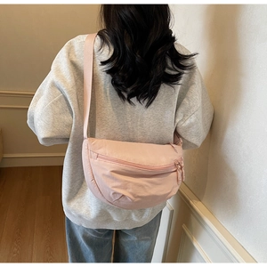 Pink crescent nylon crossbody bag shown worn by a model in a casual lifestyle setting