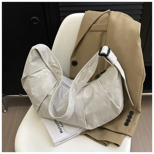 Detail of a textured beige crescent bag with adjustable strap on a white chair
