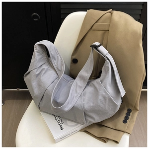 Close-up of grey pleated nylon dumpling bag with adjustable strap on white books
