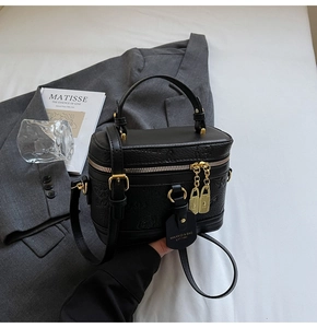 Detail of black embossed leather box bag with gold hardware and top handle on a table