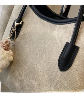 Detail der beigen Twill-Tasche mit schwarzem Lederbesatz und goldener Logoprägung