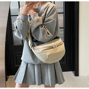 Close-up of cream nylon crescent crossbody bag worn with a casual gray sweatshirt