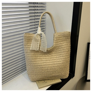 Detail der beigen Stroh-Tasche mit eleganter weißer Spitzenschleife und Webstruktur