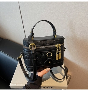 Detail of black box-shaped crossbody bag with gold hardware and embossed texture