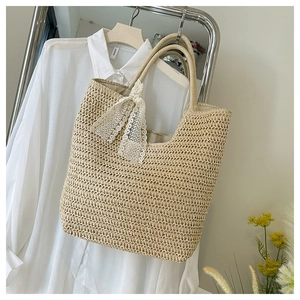 Detail der handgewebten Strohtasche mit weißer Spitzenschleife und stabilen Henkeln