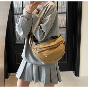Side view of a khaki nylon crescent bag worn crossbody with casual gray outfit