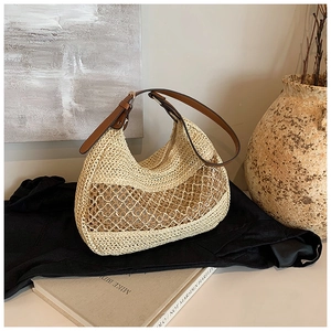Artistic detail of a hollow straw tote bag with brown leather strap in a warm setting