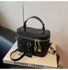 Detail view of black box bag featuring embossed patterns and gold hardware on white books