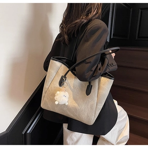Lifestyle-Ansicht einer beige Shopper-Tasche mit schwarzem Rand und weißem Pelzanhänger
