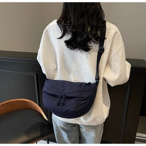 Close-up of a dark blue nylon crescent messenger bag worn by a model in a casual setting