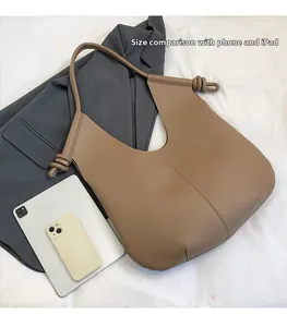 Detail view of large brown leather tote bag with knot strap showing iPad size comparison