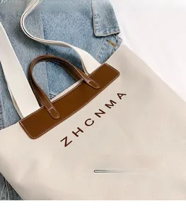 Detail of canvas tote bag showing ZHCNMA logo and dark brown leather handle stitching