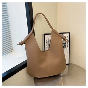 Close-up of khaki hobo bag with knotted strap detail on a minimalist metal table
