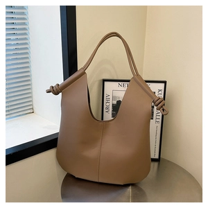 Detail of khaki large tote bag with knotted strap design on a minimalist metal table
