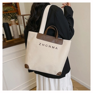 Rear view of a large canvas tote bag with brown leather trim and ZHCNMA logo on model